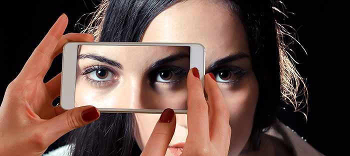 Mujer joven mostrando una parte de su rostro en la pantalla de un smartphone.